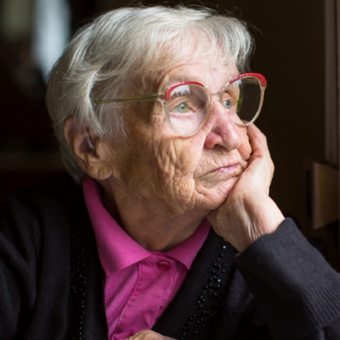 Photo of an elderly woman looking out of a window in a bad mood.
